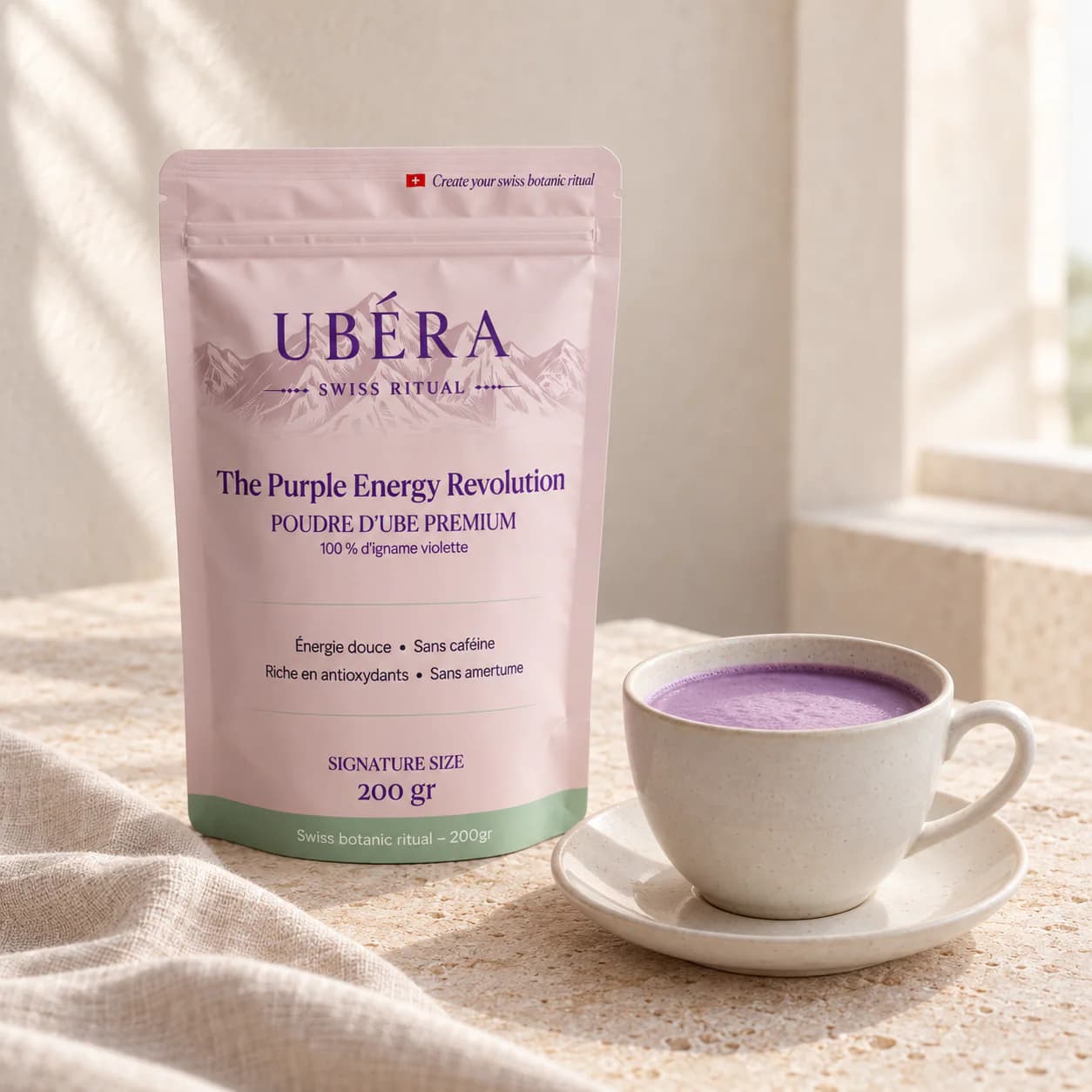 UBÉRA-Beutel 200 g und eine Keramiktasse Ube-Latte auf elfenbeinfarbenem Stein bei natürlichem Licht