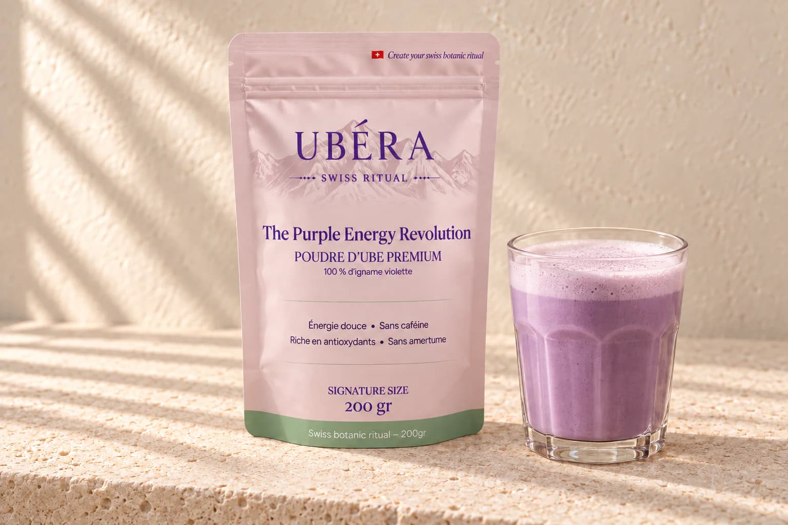 A UBÉRA 200 g pouch and an ube latte in a glass, on ivory stone