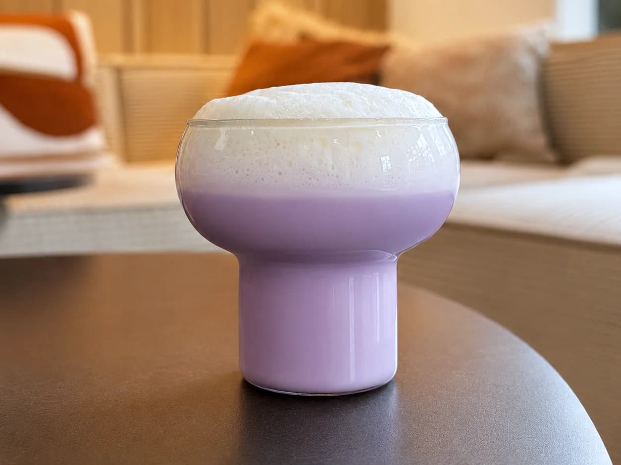 Latte à l’ube violet dans un verre, dans la lumière chaude d’un salon